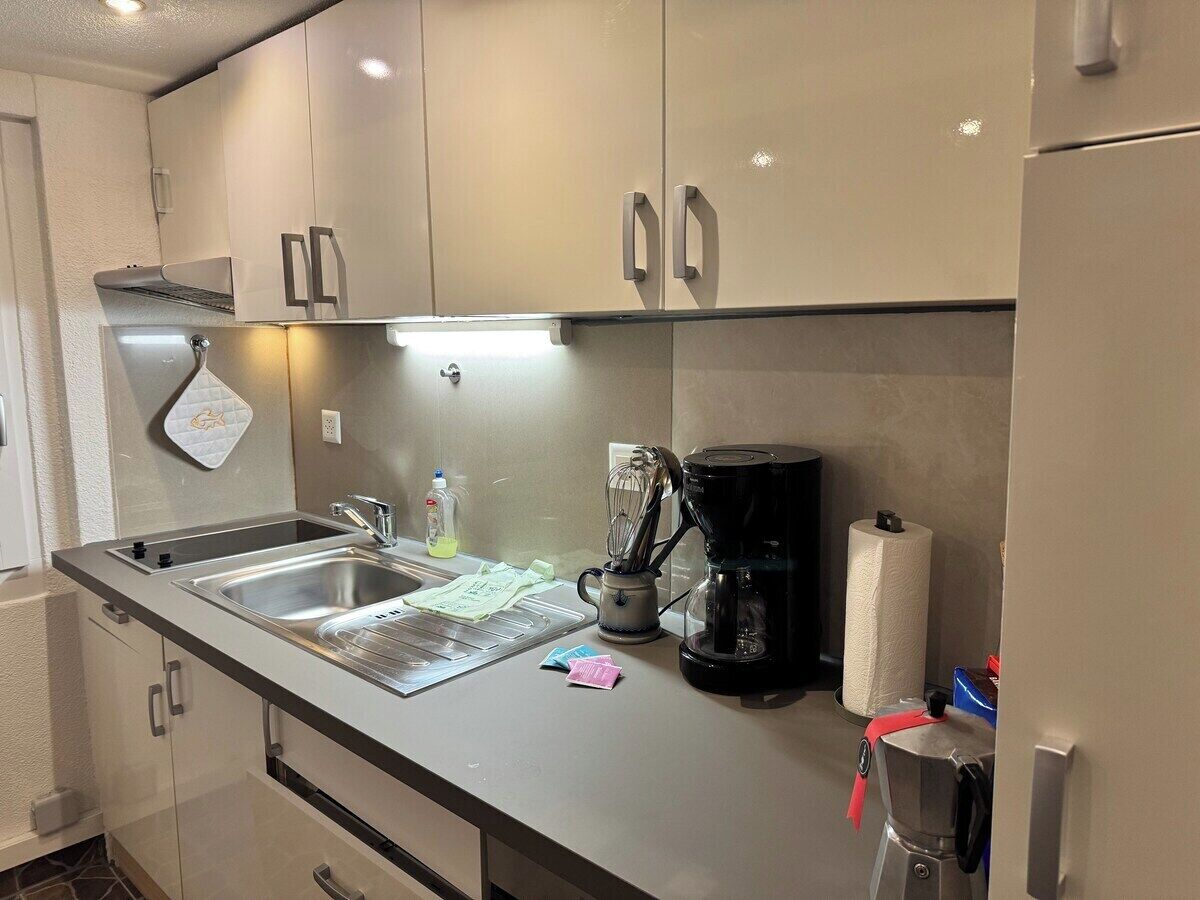 Una kitchenette con un lavamanos de acero inoxidable, una cafetera y un rollo de toallas de papel.