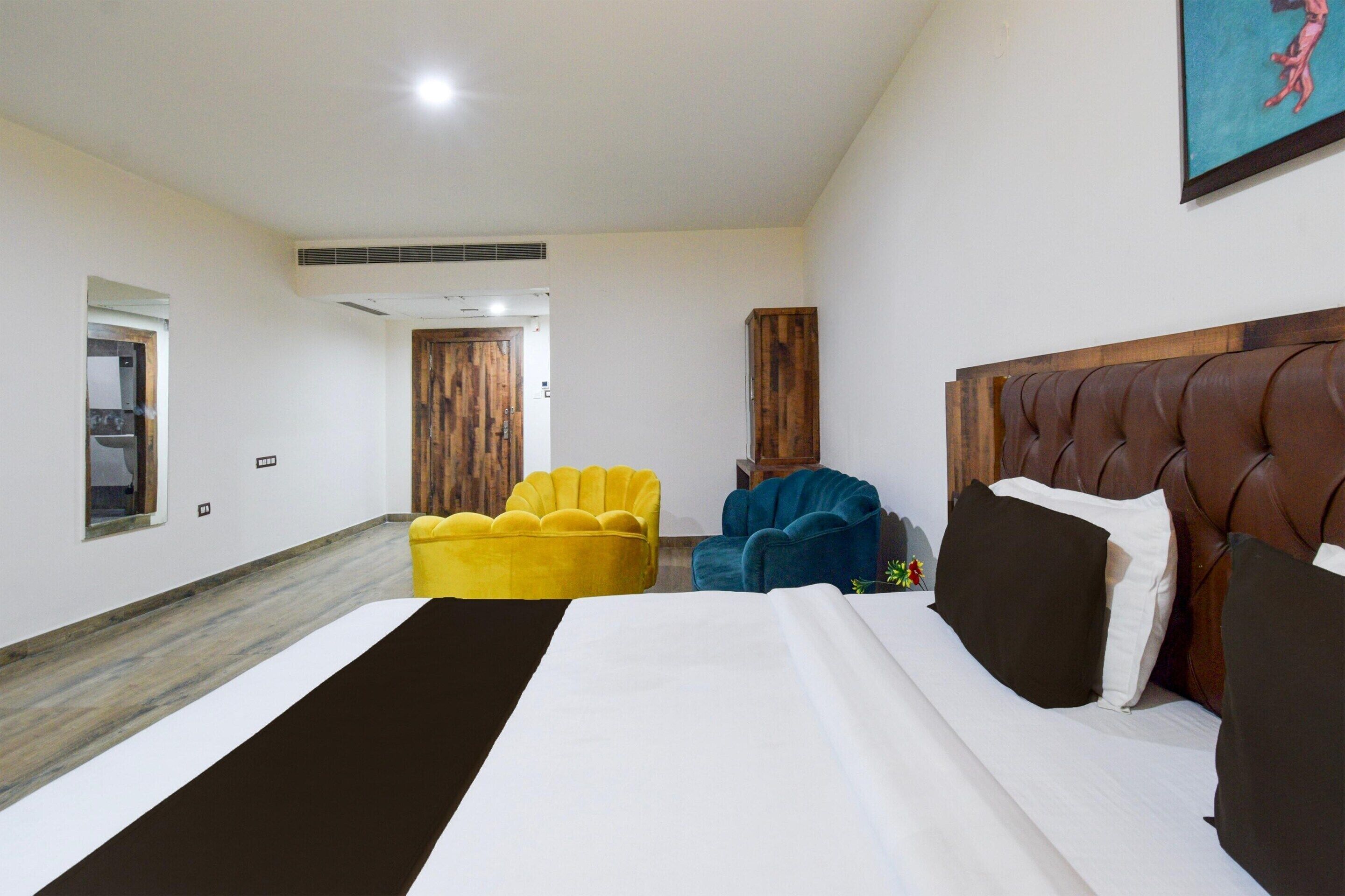 A hotel room with a large bed, a wooden headboard, a yellow armchair, a blue armchair, and a wooden door.