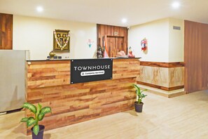 A reception desk with a sign reading 'Townhouse Company Serviced,' a wooden wall, a potted plant, and a fire extinguisher. - Deluxegrace Complex (Hyderabad)