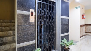 A building entrance with a metal gate, a fire exit sign, a fire extinguisher, and a potted plant. - Deluxegrace Complex (Hyderabad)