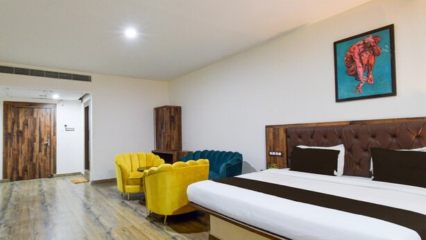 A hotel room with a large bed, a yellow armchair, a blue armchair, and a wooden wardrobe. - Deluxegrace Complex (Hyderabad)