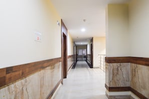 A corridor with marble flooring, wooden paneling, and a handrail on the right. - Deluxegrace Complex (Hyderabad)