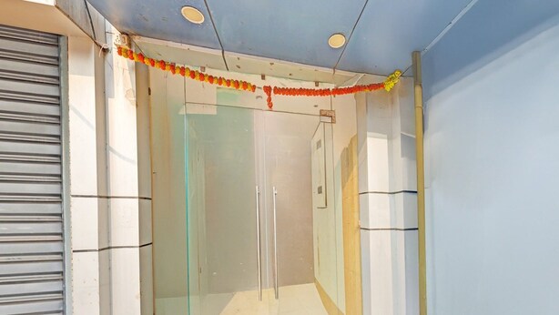 Ein verschlossener Glastür-Eingang mit einem Metallgitter links, einem gefliesten Boden und einer blauen Wand.