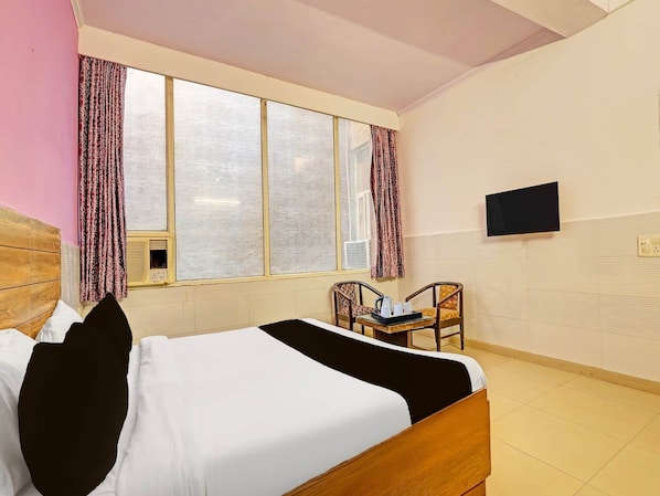 Une chambre d’hôtel comprenant un lit, un bureau avec une chaise, un téléviseur fixé au mur et une fenêtre avec des rideaux.