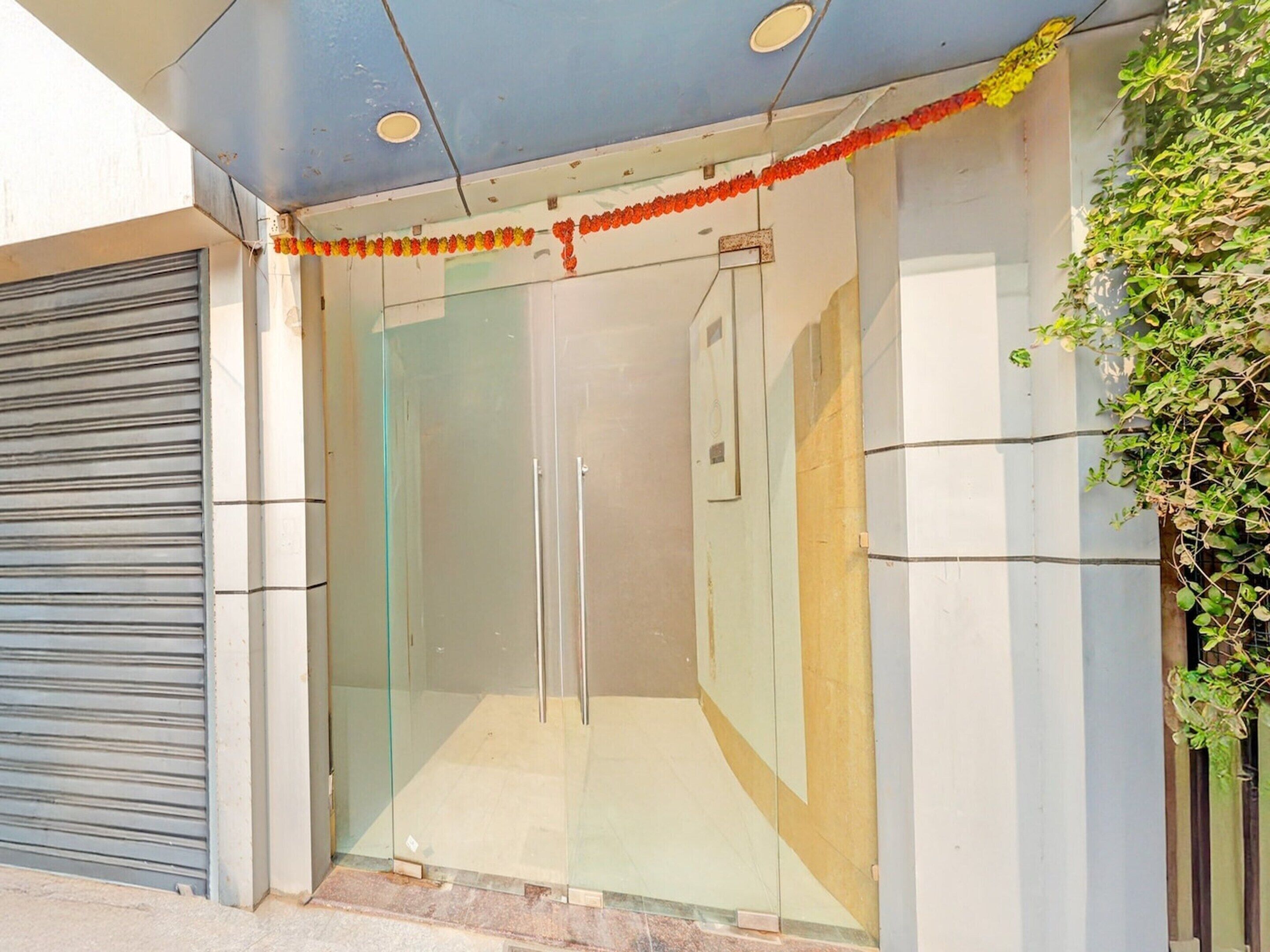 A modern building entrance with a glass door, a metal shutter to the left, and a decorative garland above the door.
