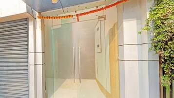 A modern building entrance with a glass door, a metal shutter to the left, and a decorative garland above the door.