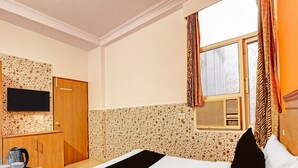 Ein Hotelzimmer mit Bett, Fernseher, Schrank, Kaffeemaschine und einem Fenster mit Vorhängen.