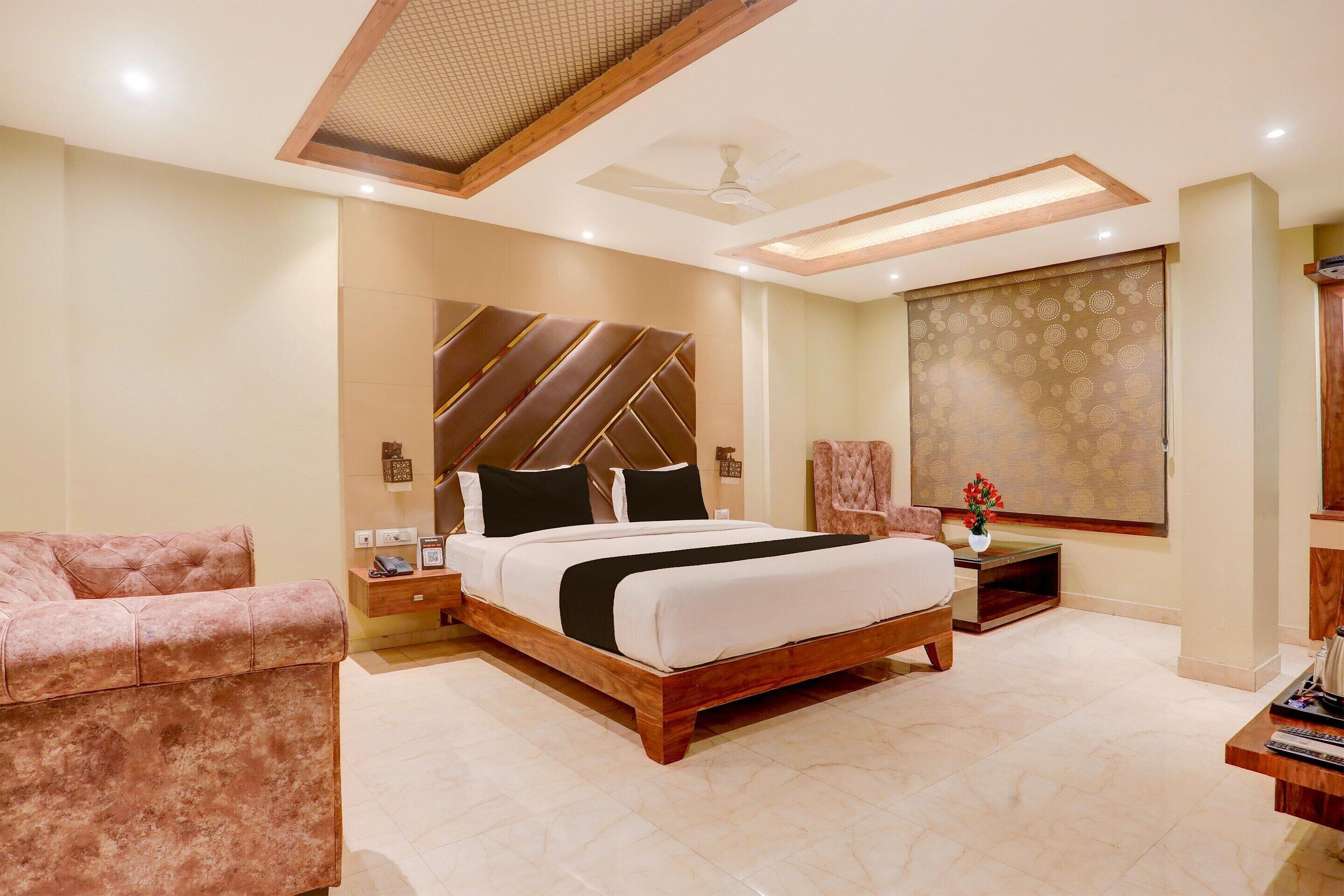 A bedroom with a large bed, a sofa, a bedside table, a nightstand, a wall-mounted TV, and a large window with a view.
