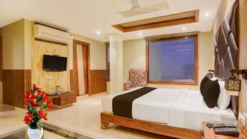 A hotel room with a bed, a TV, a desk with a phone, a vase with flowers, and a window.
