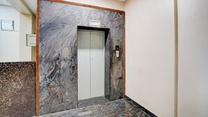 An elevator with marble walls and a wooden frame, a control panel, and a sign above the door.