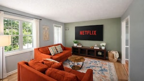 Een woonkamer met een bank, een salontafel, een flatscreen-tv en een groot raam.