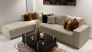 A modern living room with a sectional sofa, a black coffee table with candles, and a large abstract painting on the wall. - Absolute Comfort in a Luxury Residence, Soukra (Tunis)
