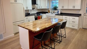 A modern kitchen with white cabinets, a wooden island, bar stools, and pendant lighting. - Tranquil forest retreat - 3br / 2ba - quiet beautiful desired neighborhood (Flagstaff)