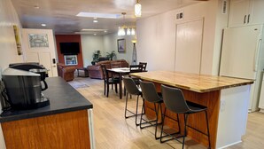 A kitchen with a wooden island, bar stools, a coffee maker, and a dining area with chairs and a table. - Tranquil forest retreat - 3br / 2ba - quiet beautiful desired neighborhood (Flagstaff)