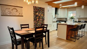 A modern kitchen with white cabinets, a wooden ceiling, and a dining area with a table and chairs. - Tranquil forest retreat - 3br / 2ba - quiet beautiful desired neighborhood (Flagstaff)