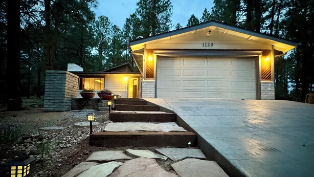 A two-story house with a garage, stone steps leading to the entrance, and a well-lit driveway. - Tranquil forest retreat - 3br / 2ba - quiet beautiful desired neighborhood (Flagstaff)