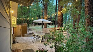 An outdoor patio with a table and chairs, surrounded by trees and string lights. - Tranquil forest retreat - 3br / 2ba - quiet beautiful desired neighborhood (Flagstaff)