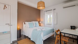 A bedroom with a bed, bedside table, lamp, and a desk with a chair.