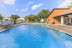 A swimming pool with a wooden deck, a covered area with seating, and a fenced area with a sign. - Landing Apartments Near CVC (DeSoto)