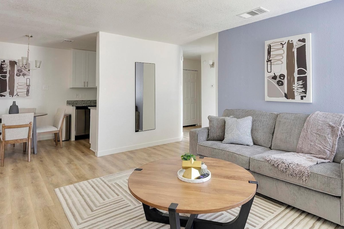A modern living room with a grey sofa, a wooden coffee table, and a dining area with a table and chairs.