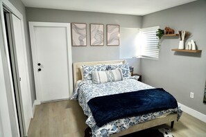 A bedroom with a bed, a door, wall art, and a window with blinds. - Hollywood 3801 (Hollywood)