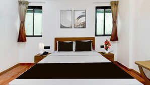 Ein Hotelzimmer mit einem großen Bett, zwei Nachttischen, einer Wandlampe und zwei mit Vorhängen versehenen Fenstern.