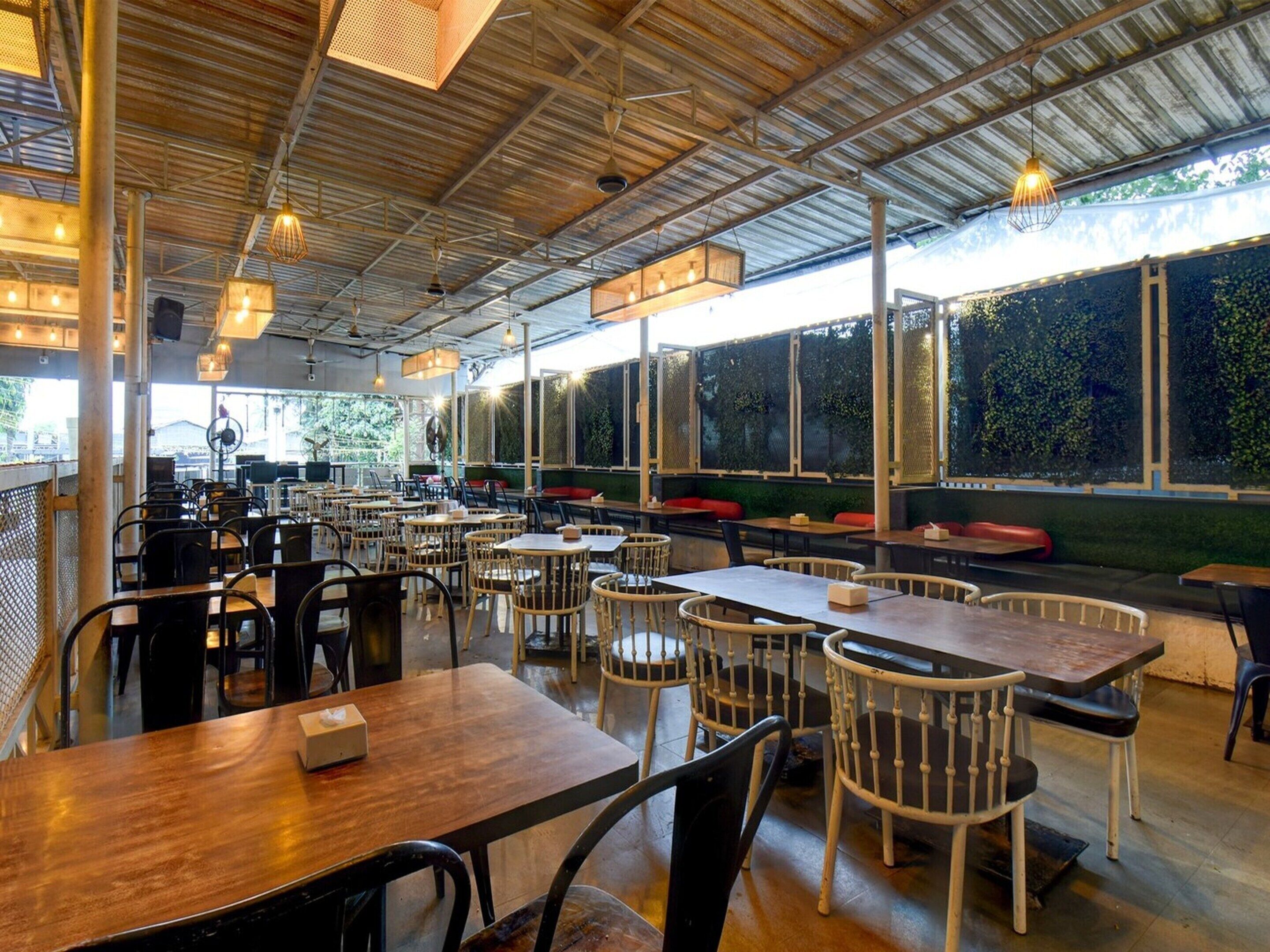 Un restaurant spacieux avec de hauts plafonds, des poutres apparentes et de grandes fenêtres. Les tables et les chaises sont disposées pour accueillir les clients.