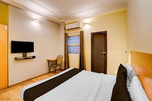 A hotel room with a bed, a desk, a chair, a television, and an air conditioning unit. - Deluxe Hotel Sunshine (Lucknow)