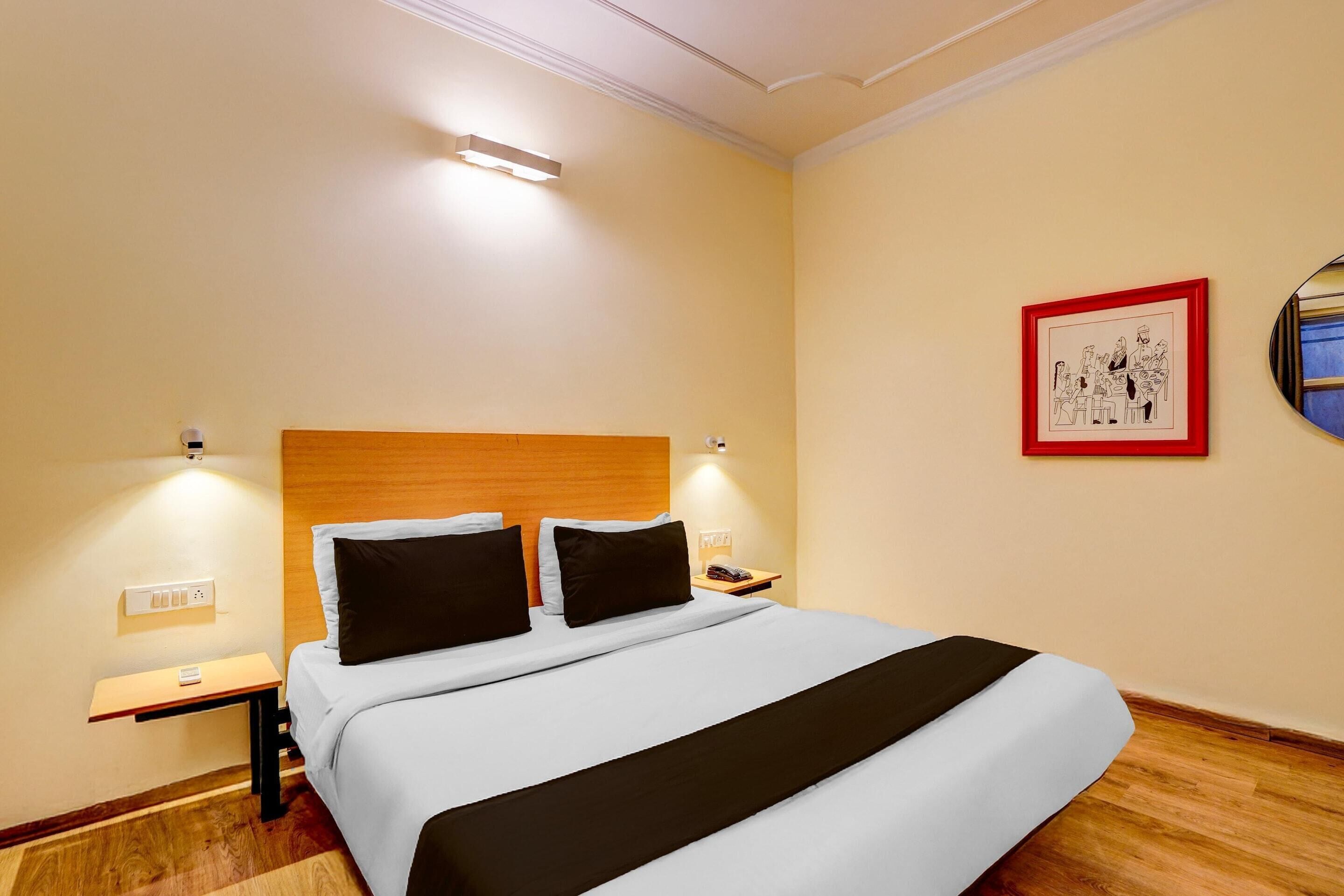 Een hotelkamer met een bed, nachtkastjes, een lampje aan de muur en een lijst met een afbeelding.