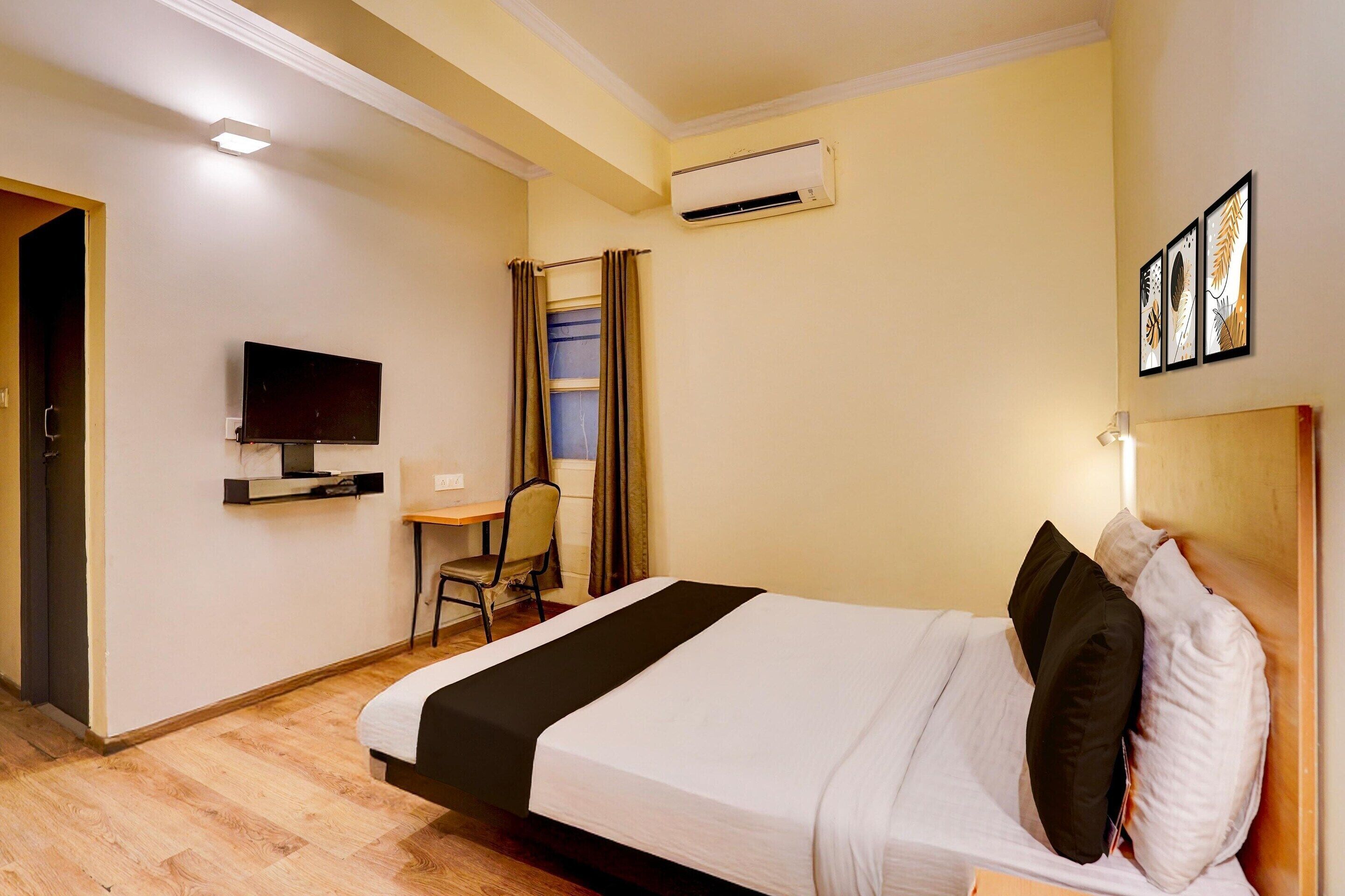 Une chambre d’hôtel comprenant un lit, un bureau avec une chaise, une télévision, un appareil de climatisation et une fenêtre avec des rideaux.