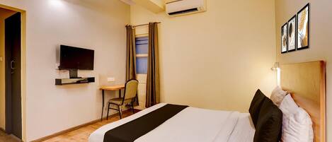 Une chambre d’hôtel comprenant un lit, un bureau avec une chaise, une télévision, un appareil de climatisation et une fenêtre avec des rideaux.