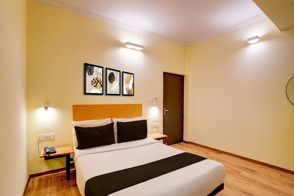 A hotel room with a bed, bedside tables, a wooden headboard, a door, and wall-mounted artwork. - Deluxe Hotel Sunshine (Lucknow)