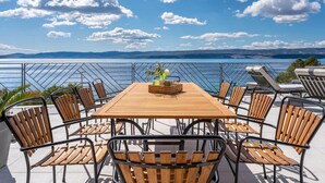 A wooden table with chairs, a basket, and a potted plant on a terrace with a view of a body of water and distant hills. - Estate With Jacuzzi, Gym (Omis)