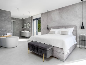 Un dormitorio moderno con una cama grande, una bañera y una ducha a ras de suelo.