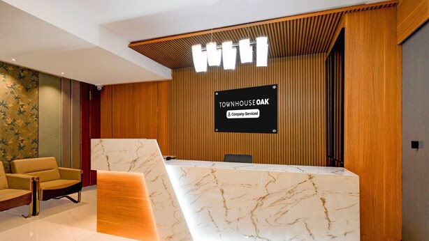 A reception desk with a marble top, wooden paneling, and a sign indicating 'Townhouse Oak' as a company-serviced location. - Deluxekhajaguda Premium Suites (Hyderabad)