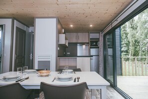 A modern kitchen with built-in appliances, a dining table set for four, and a large sliding glass door leading to an outdoor deck. - Villa (Malansac)