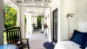 A covered porch with a table, chairs, and a bed.