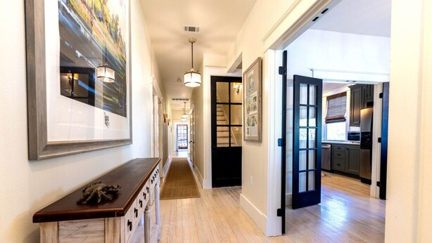 A hallway with wooden floors, a bench, framed artwork, and a kitchen area with cabinets and appliances.