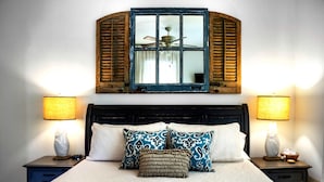 Una cama con cabecera, dos lámparas de noche y un ventanal con contraventanas.