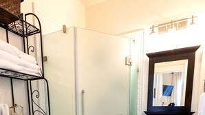 Un baño con inodoro, ducha, lavamanos con espejo y un perchero para toallas.