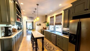 A modern kitchen with a central island, stainless steel appliances, and a view to the dining area. - Book a Memory Presents the Pontchartrain Villa - Walk to the Lake (Mandeville)