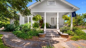 A white two-story house with a porch, surrounded by lush greenery and a gravel pathway. - Book a Memory Presents the Pontchartrain Villa - Walk to the Lake (Mandeville)