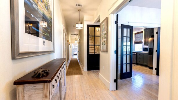 A hallway with wooden floors, a bench, framed artwork, and a kitchen area visible through an open door. - Book a Memory Presents the Pontchartrain Villa - Walk to the Lake (Mandeville)
