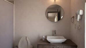 A bathroom with a toilet, a sink, a mirror, and a hairdryer. - Milan Providencia Studio (Guadalajara)