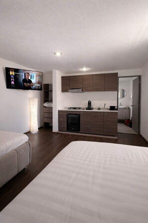 Ein modernes Hotelzimmer mit Bett, Fernseher, Küchenzeile und Bad.