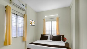 A bedroom with a bed, two windows with curtains, an air conditioning unit, and a small table with a vase. - Deluxe Nagpur Royal (Nagpur)
