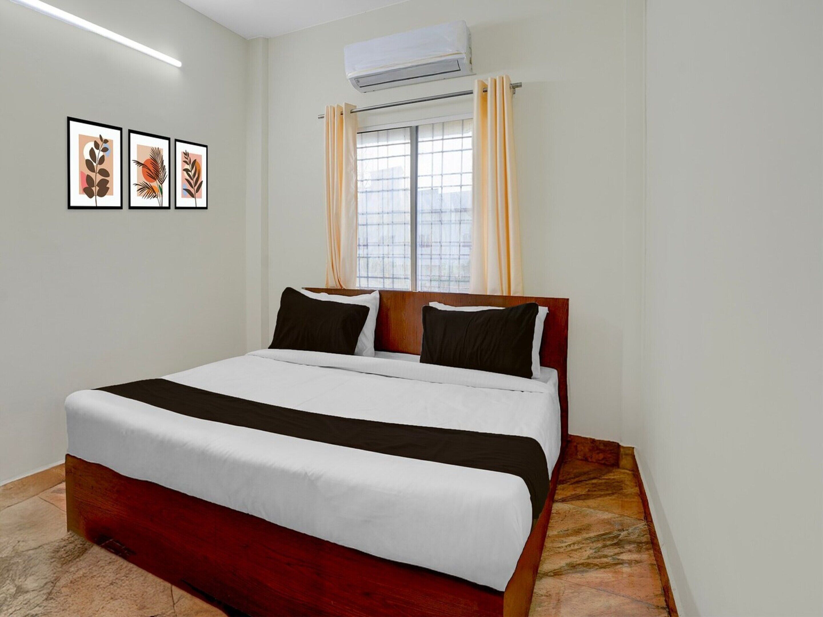 A hotel room with a bed, air conditioning unit, window with curtains, and artwork on the wall.