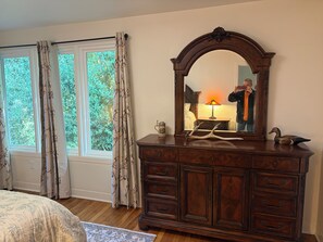 Une chambre à coucher avec une commode en bois, un miroir, une lampe et une fenêtre avec des rideaux.