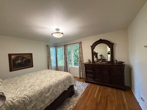 A bedroom with a bed, dresser, mirror, and windows.