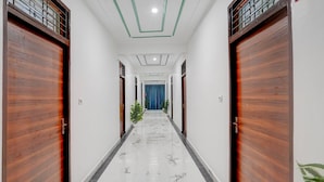 A hallway with wooden doors, a marble floor, and a blue curtain at the end. - Deluxebellandur Near Embassy Tech Village (Bakshi Ka Talab)